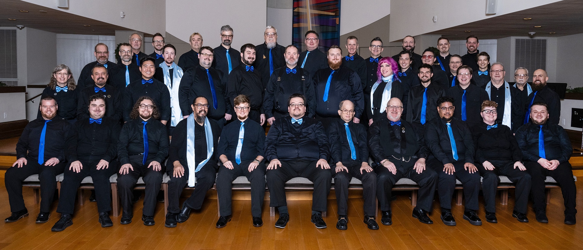 Formal group photo of Perfect Harmony Chorus taken at the December 2023 concert. Approximately 40 singers are pictured wearing formal black attire with blue ties.